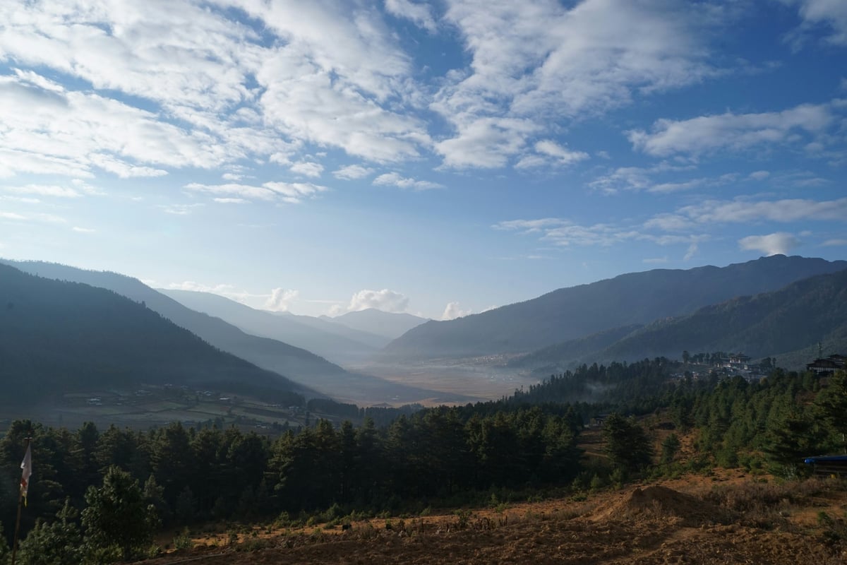 A mountainous landscape in Bhutan, with a valley in the distance and a small Phobjikha in the foreground.